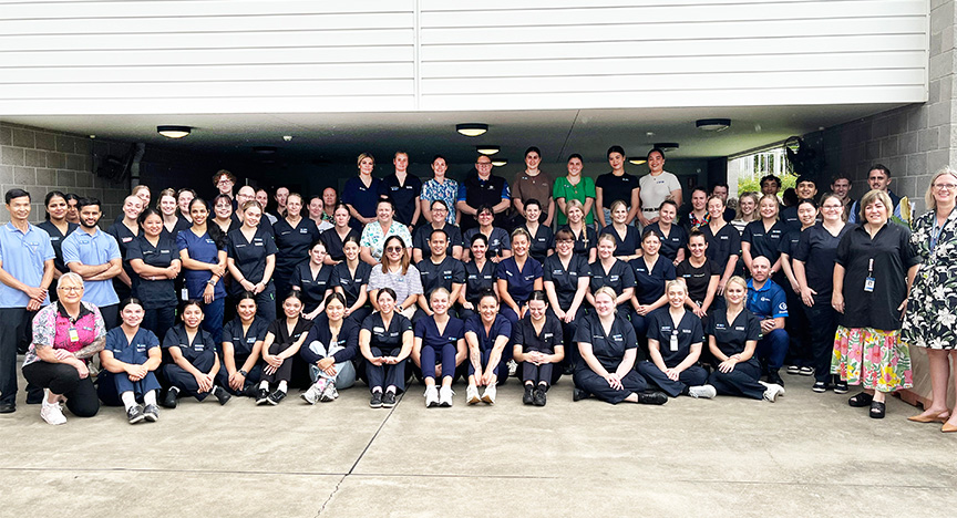 Very large group of nurses, most wearing navy scrubs, stand and sit in a big group photo on their first day of orientation, in an undercover outside area of the hospital’s learning and development centre.