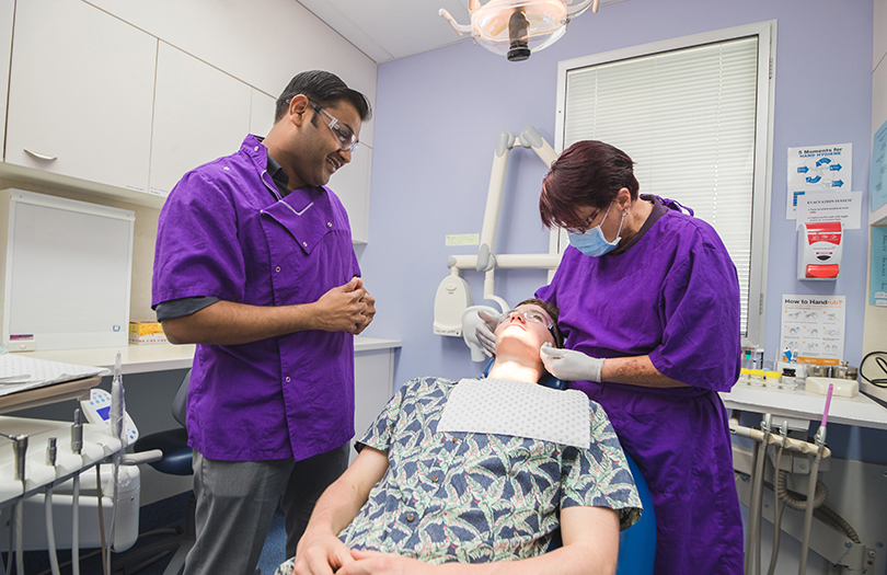 Two dentists from CQ Health examine patient in dental chair.