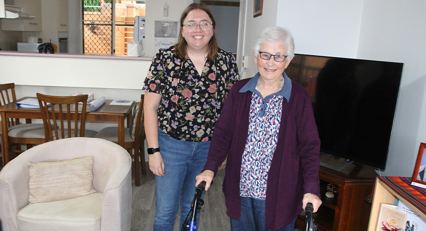 Transition Care Program Senior Social Worker Beth Ford stands smiling with patient Desma Clarke in her living room.