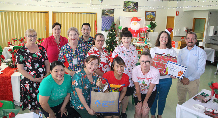 Second place winners at North Rockhampton Nursing Home standing in a decorated dining room and receiving their prize hamper.