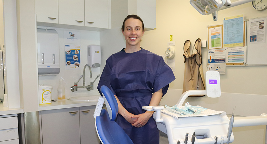 Dr Stevie, Senior Dentist from CQ Health stands smiling in a dentist's office.