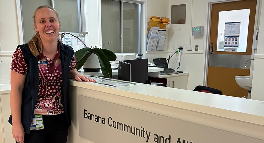 Healthcare worker looking happy and resting her arm on a reception desk.