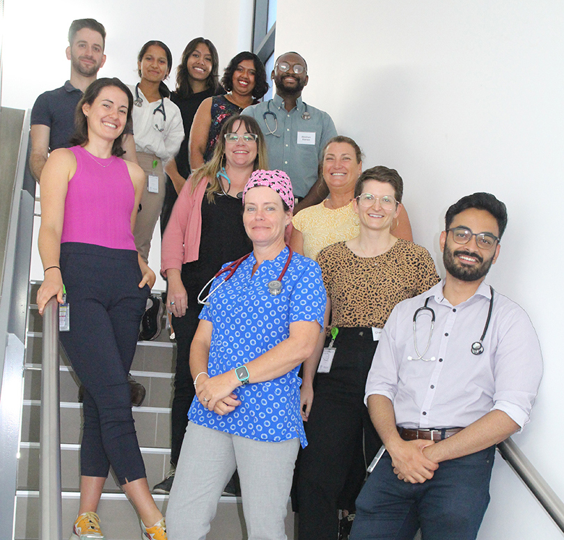 A group of smiling medical interns from CQ Health, representing a mix of genders and ethnicities, stand in a hospital stairway.